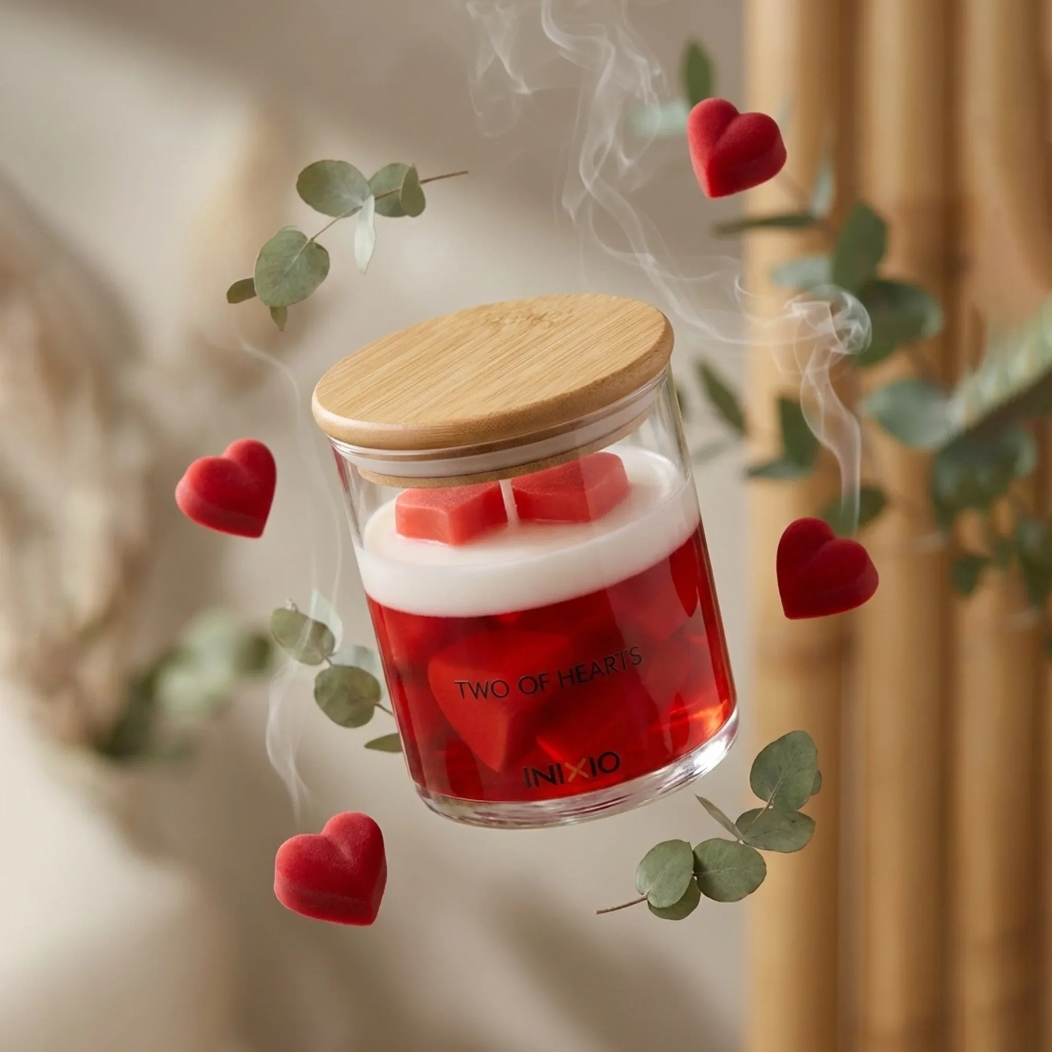 Heart-shaped scented soy wax candle in glass jar with wood lid, surrounded by red hearts and eucalyptus
